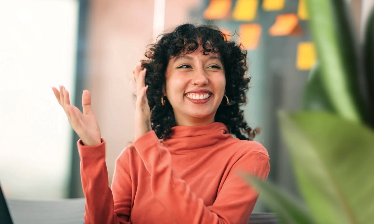 Woman in orange shirt smiling and clapping.