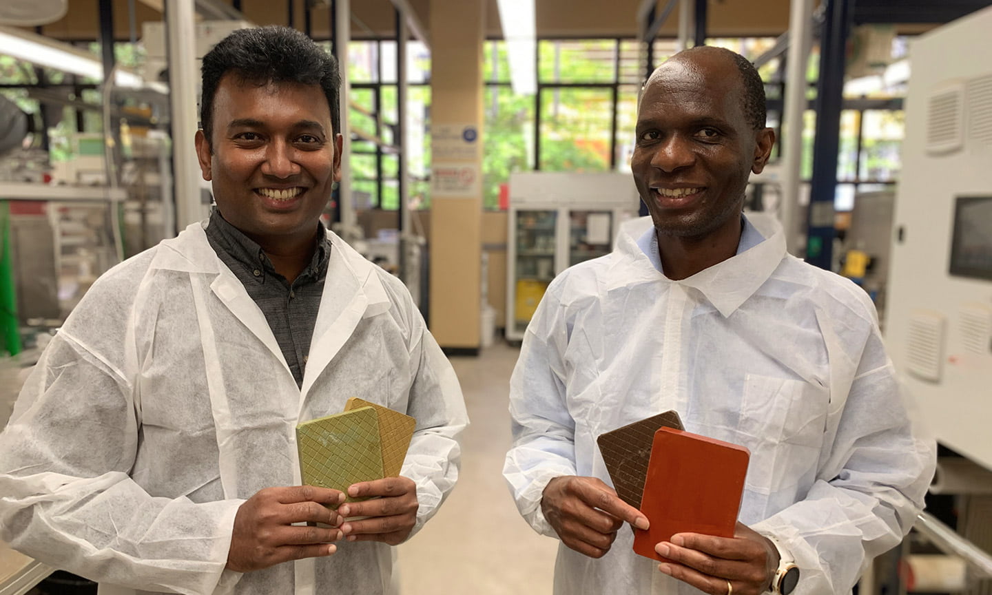 Two RMIT researchers stand smiling in protective clothing holding their sustainable building cladding samples