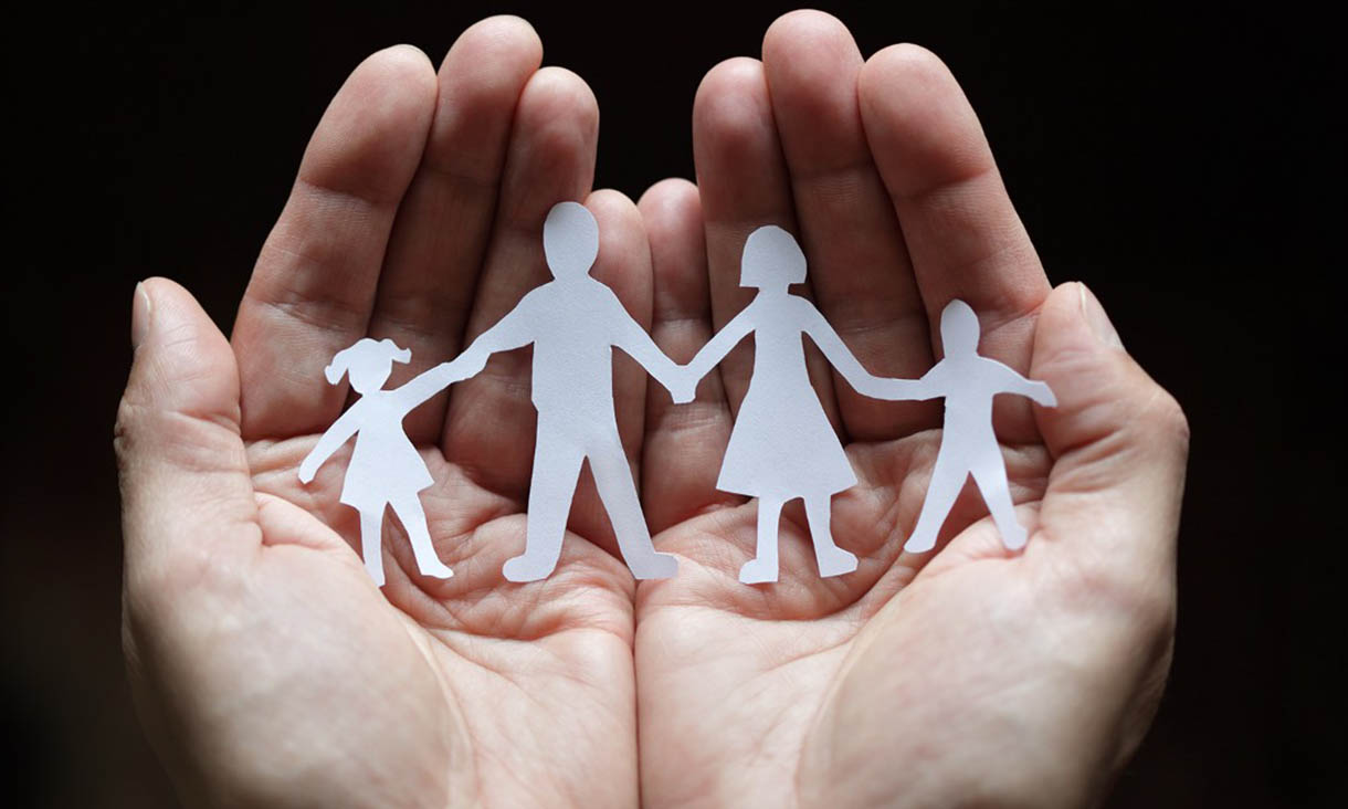 Hands hold white paper cutout of two children and two adults