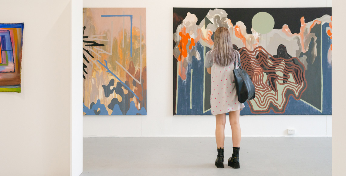 Female student standing in front of large art piece in an art gallery