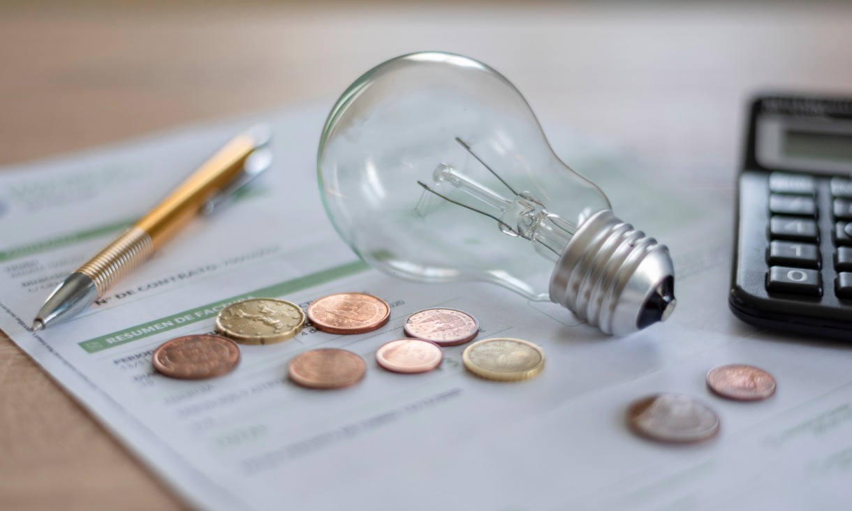 Electricity bill with light bulb, several coins, calculator and pen on the desk. Concept of electricity prices and tax payments.